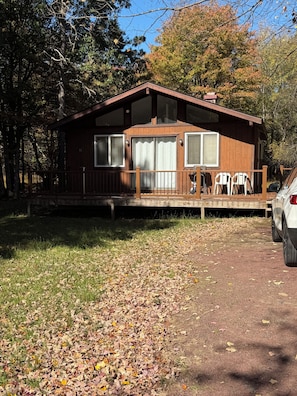 A cabin with a deck, a covered porch, and a car parked in front.