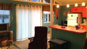 A compact living space with a dining area, kitchenette, and a large window providing natural light.