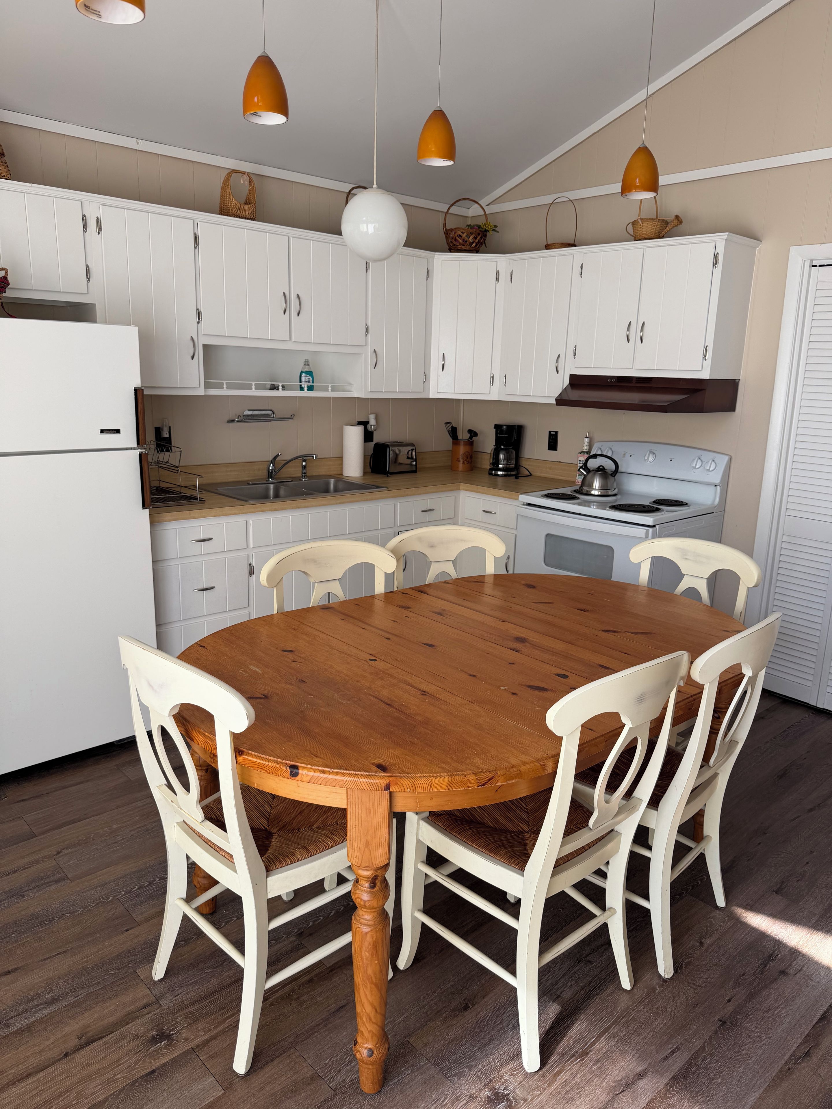 A kitchen with white cabinets, a wooden dining table, and white chairs.