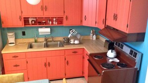 A compact kitchen with a sink, stove, and red cabinets.