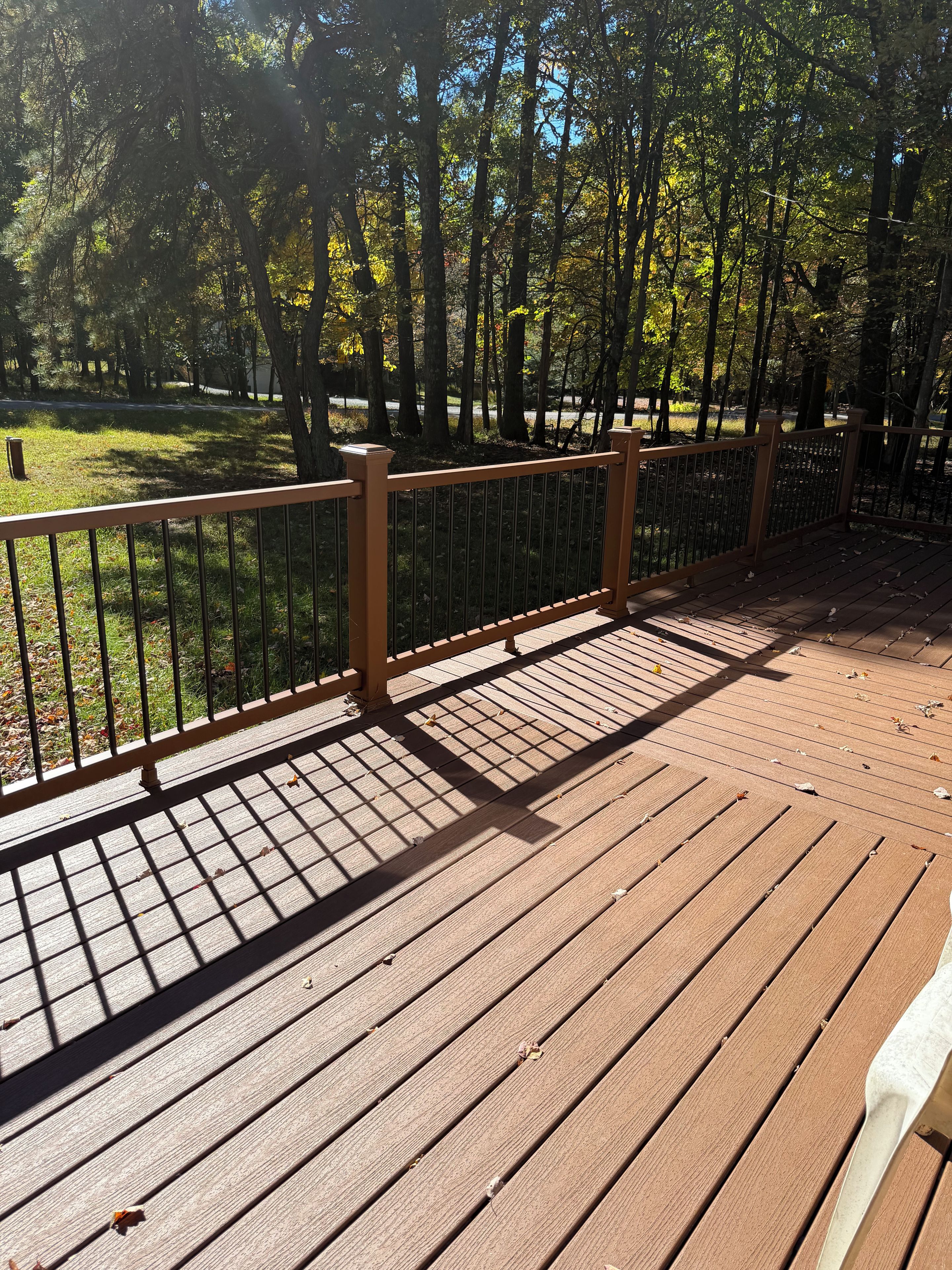 A wooden deck with a metal railing, surrounded by trees and grass.