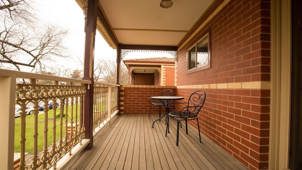 A covered outdoor area with a wooden deck, a brick wall, and a metal railing.
