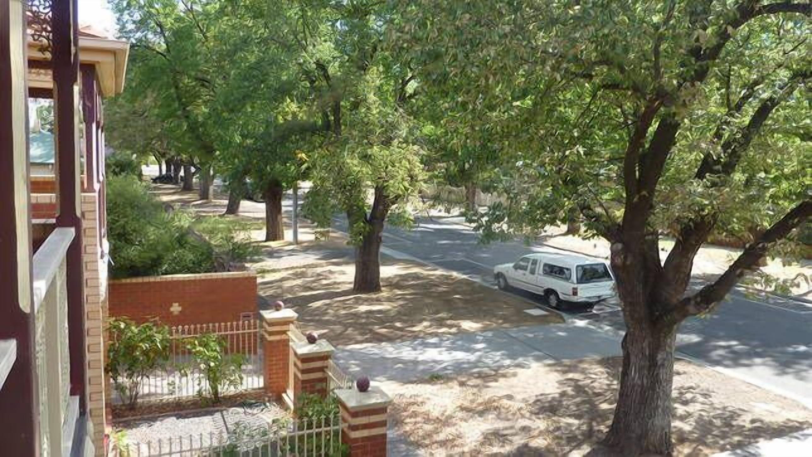 Une rue résidentielle bordée d’arbres, avec un fourgon blanc et un bâtiment en briques.