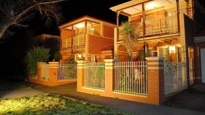 A two-story house with a balcony, a fenced yard, and a well-lit exterior at night.