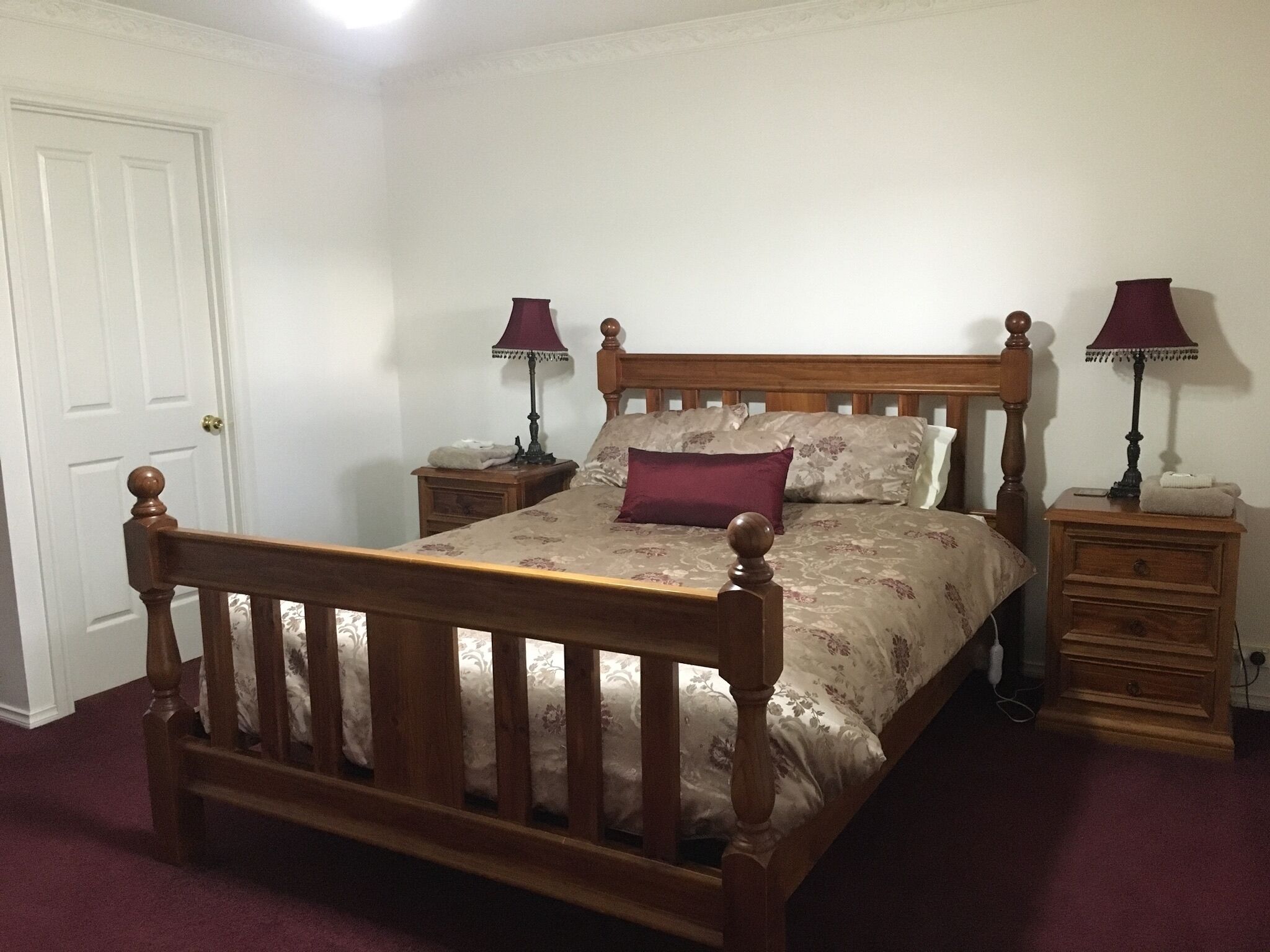 A bedroom with a wooden bed, two bedside tables, a nightstand, a door, and a carpeted floor.
