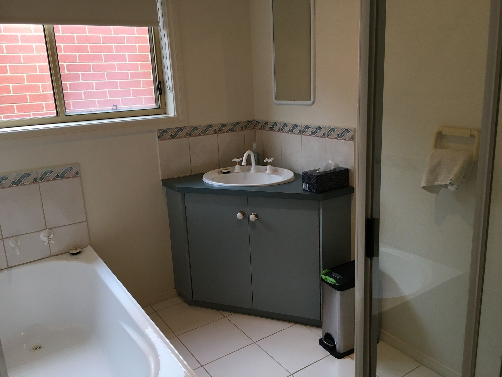 A bathroom with a white bathtub, a sink with a mirror above it, and a trash bin.