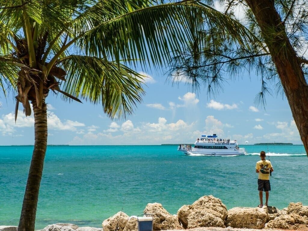 A person standing by a rocky shore with a boat in the distance.