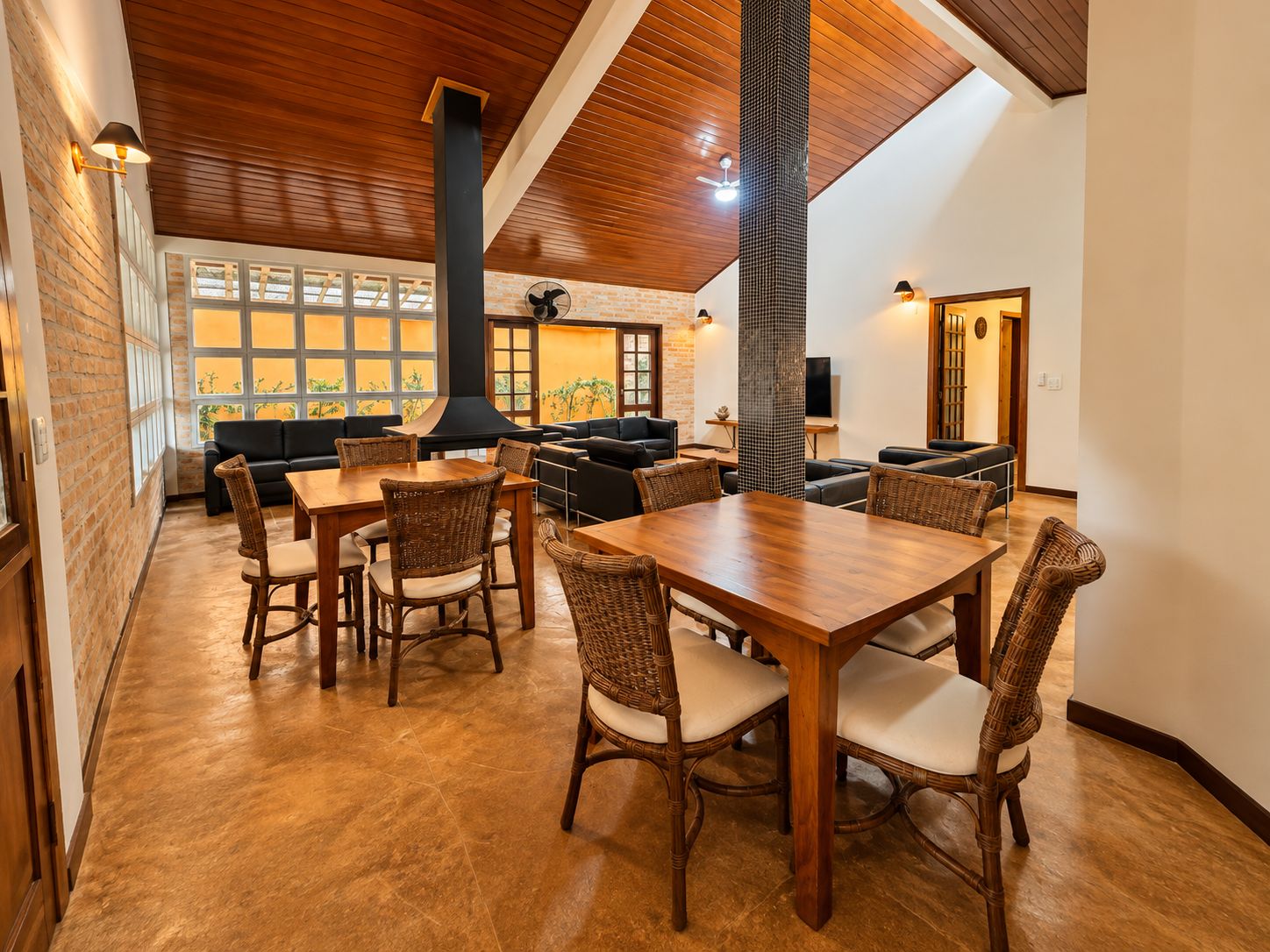 A dining area with wooden tables and chairs, a brick wall, and a large window with a view.