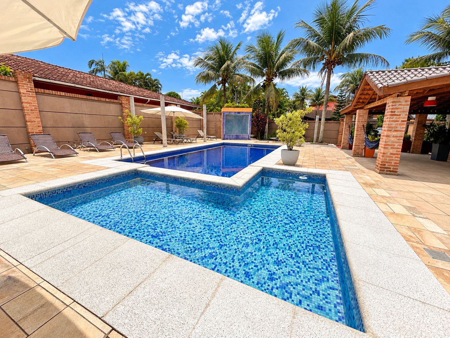 A rectangular pool with a tiled edge, surrounded by lounge chairs and potted plants, under a clear sky.