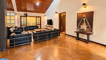 A spacious living area with a high ceiling, a fireplace, a television, and a large painting.