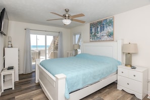 A bedroom with a bed, a nightstand, a lamp, a ceiling fan, and a painting.