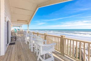 A wooden deck with white chairs overlooking a beach.