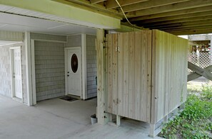 Uma área externa coberta com estrutura de madeira, uma porta e piso de concreto.