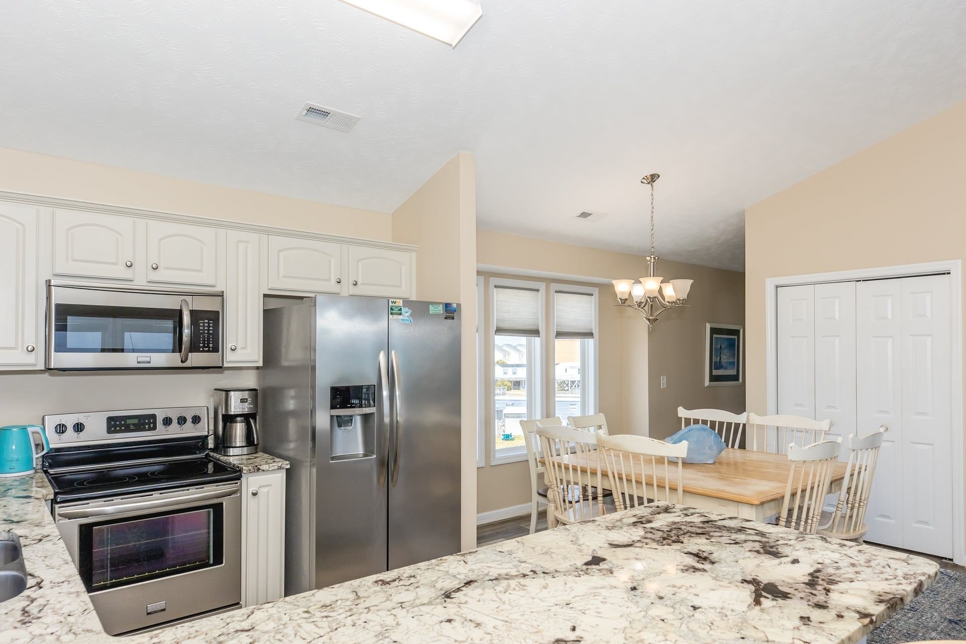 A kitchen with stainless steel appliances, a marble countertop, and a dining area with a chandelier.
