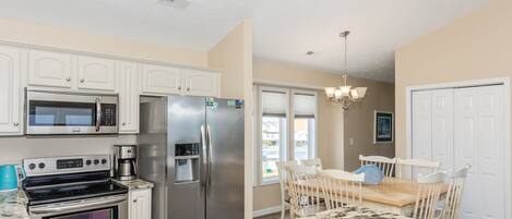 A kitchen with stainless steel appliances, a marble countertop, and a dining area with a chandelier.