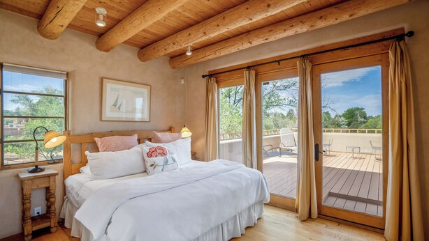 A bedroom with a wooden ceiling, a bed with white bedding, a nightstand with a lamp, and a large window with curtains. - Casa Don Miguel | Stylish Retreat (Santa Fe)