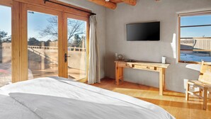 A bedroom with a large bed, a wooden desk, a chair, a TV, and a sliding glass door leading to an outdoor area. - Casa Don Miguel | Stylish Retreat (Santa Fe)