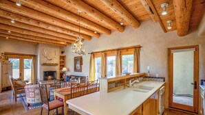 A rustic kitchen with wooden beams, a fireplace, and a dining area with chairs and a table. - Casa Don Miguel | Stylish Retreat (Santa Fe)