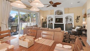 A spacious living room with a large sofa, a dining table, and a fireplace. There is a balcony with curtains and a view of the outside. - Adorable Home less then a Block to Gulf W/Private heatable Pool! (Destin)