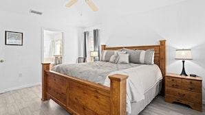 Een slaapkamer met een houten bed, een nachtkastje, een plafondventilator en een nachtlampje.