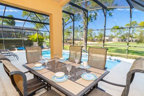 An outdoor dining area with a pool view, featuring a table set with plates, glasses, and chairs.