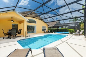 Una piscina interior con techo de vidrio, sillas junto a la piscina y una mesa.