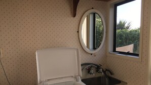 A compact bathroom with a toilet, sink, and window. - Riverfront Cottage Waipu (Waipu)