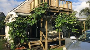 A two-story house with a wooden deck and a covered porch. - Riverfront Cottage Waipu (Waipu)