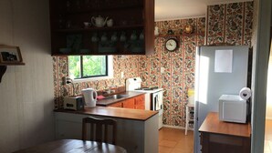 A compact kitchen with a wooden table, a sink, and a refrigerator. - Riverfront Cottage Waipu (Waipu)