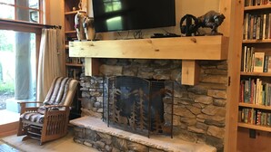 A cozy living room with a stone fireplace, a mounted television, and a bookshelf filled with books.