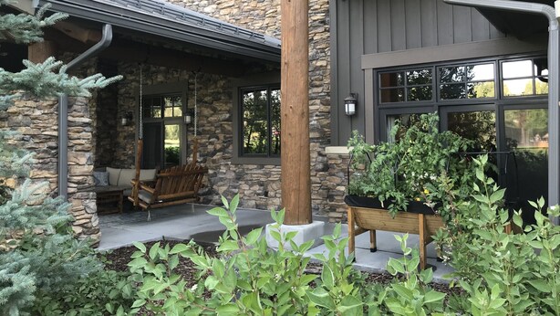 A stone building with a porch, wooden furniture, and potted plants.