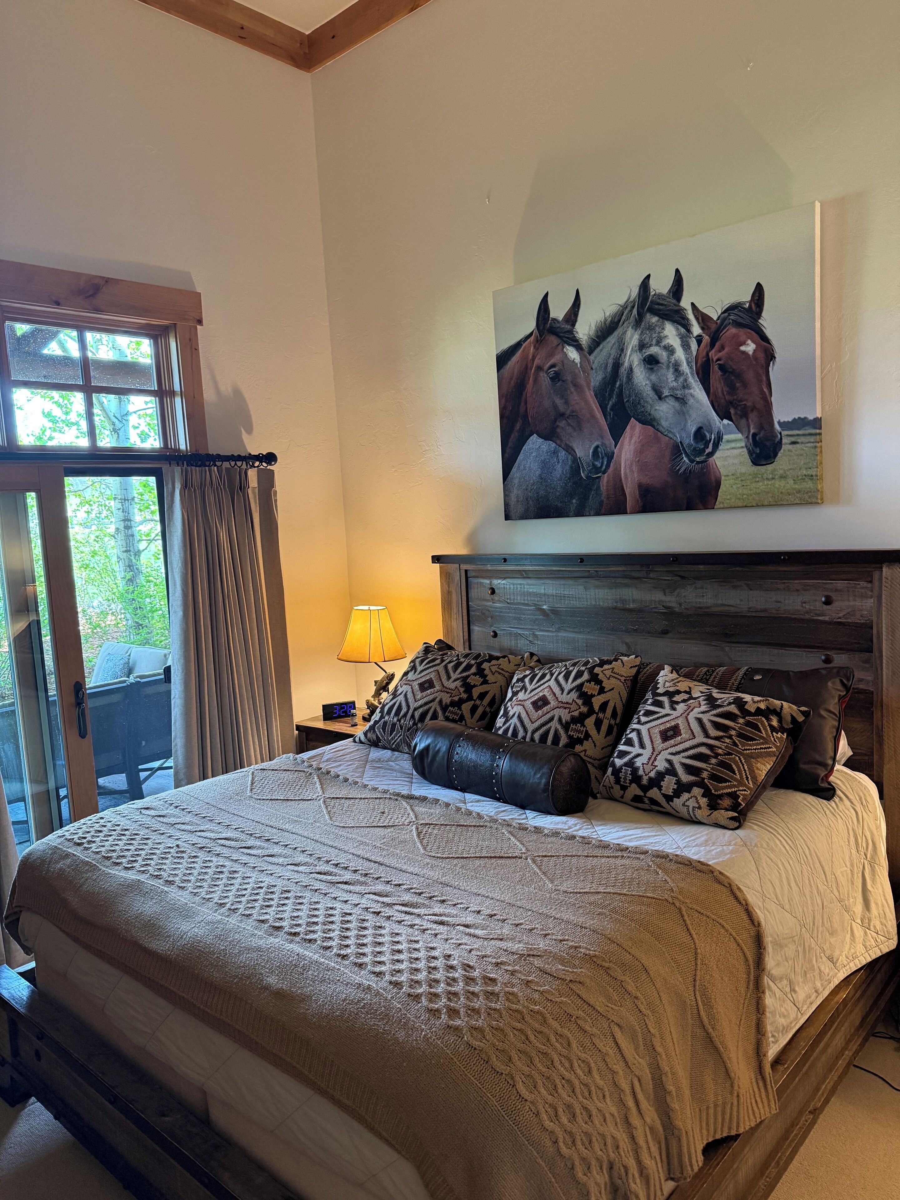 Un dormitorio con una cama, un cuadro de caballos, una lámpara y vistas por una ventana.