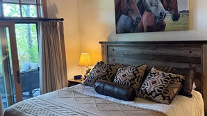 A bedroom with a bed, a painting of horses, a lamp, and a view through a window.