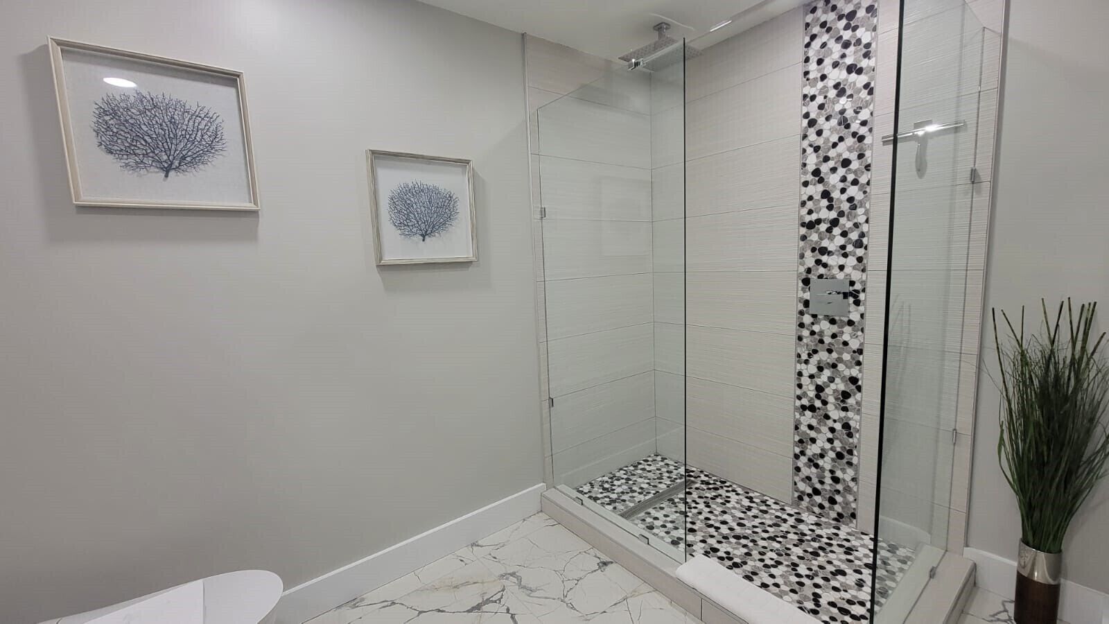 A modern bathroom with a glass shower enclosure, a marble floor, and two framed wall art pieces.