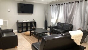 A modern living room with a black leather sofa, a coffee table, and a flat-screen TV mounted on the wall. - Private 4BR Heated Pool & Spa Home • Pet Friendly • Near Beaches (Margate)