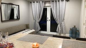 A hotel room with a sofa, a dining table with candles, a mirror, and a sliding glass door with curtains. - Private 4BR Heated Pool & Spa Home • Pet Friendly • Near Beaches (Margate)