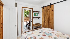 Une chambre avec un lit, une porte en bois, une porte coulissante de style grange, une petite table avec des paniers et une vue sur une terrasse extérieure.