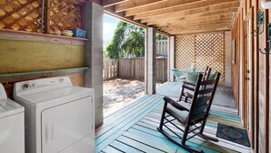 Un espace buanderie équipé d’un lave-linge et d’un sèche-linge, un fauteuil à bascule et une terrasse en bois donnant sur une cour clôturée.