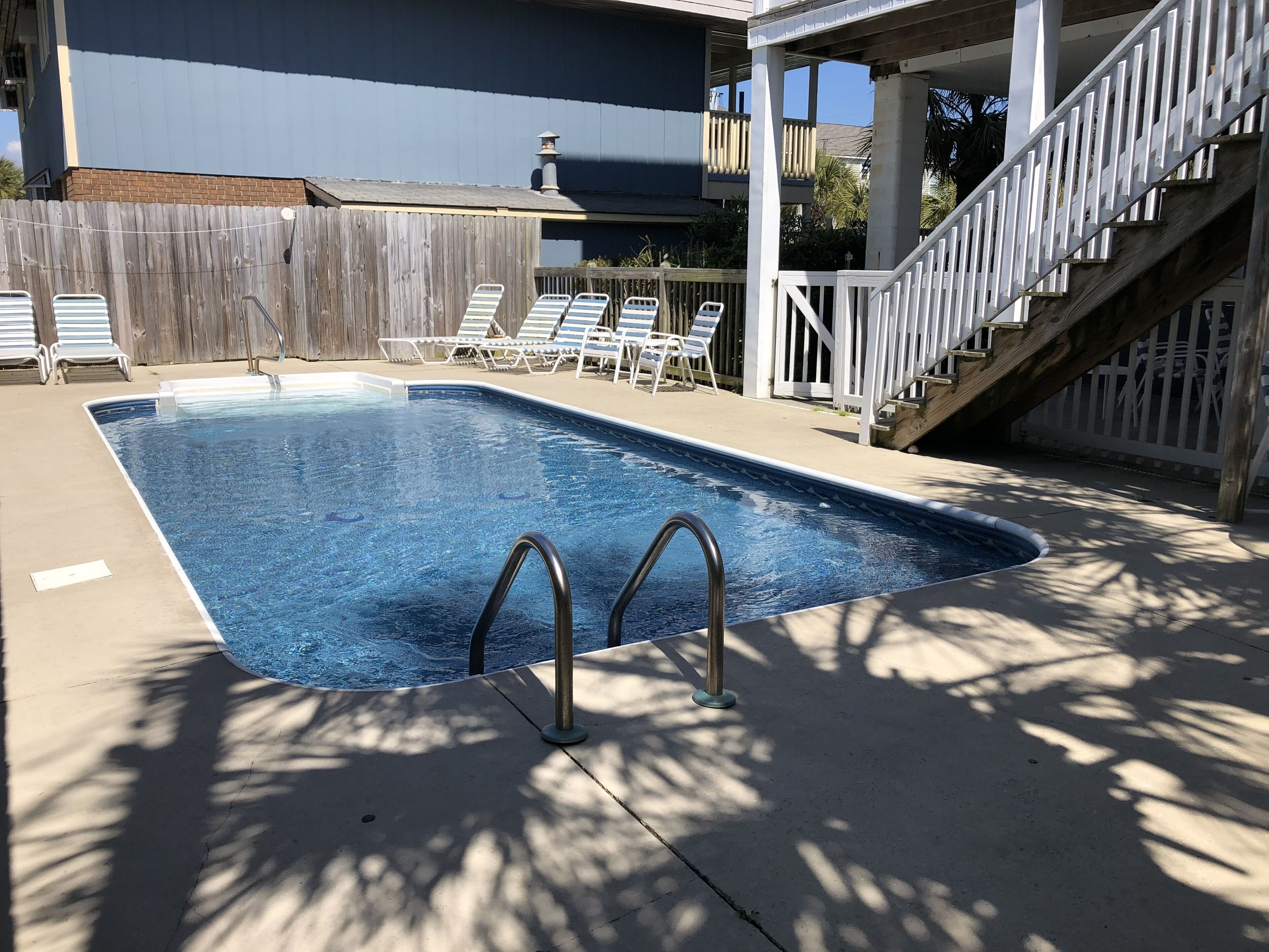 Une piscine rectangulaire dotée de deux échelles en métal, entourée d’une terrasse en bois et de rampes blanches.