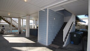 Ett takförsett utomhusområde med en trappa som leder upp till en inglasad veranda, en pool och en soptunna.