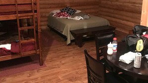 A cabin-style room with a bunk bed, a small table with chairs, and a bed with a blanket and pillows. - Cabin 7 (Garden City)