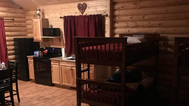 A cozy cabin interior with wooden walls, a kitchen area, a bunk bed, and a dining table. - Cabin 7 (Garden City)