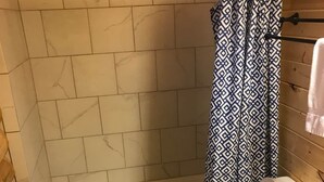 A bathroom with a white bathtub, a toilet, and a wooden vanity. - Cabin 7 (Garden City)