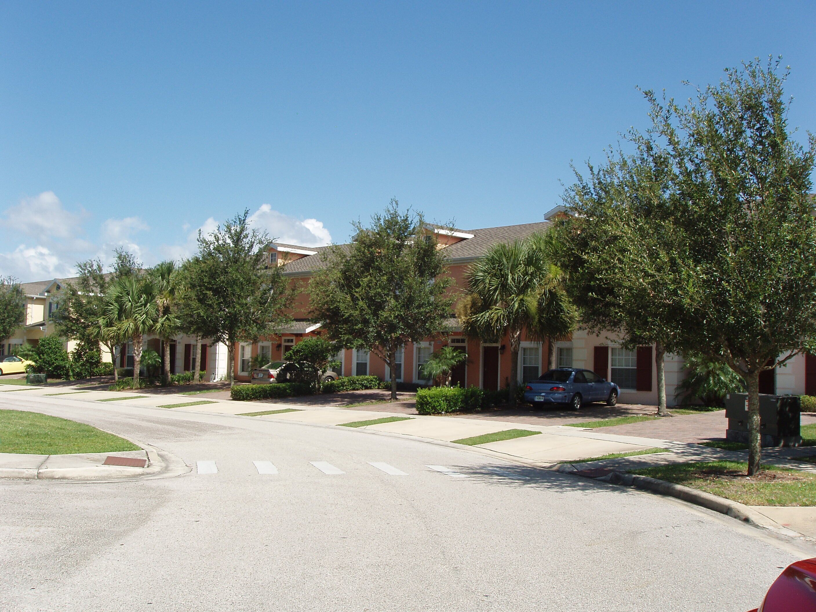 A residential street with houses, trees, and parked cars.