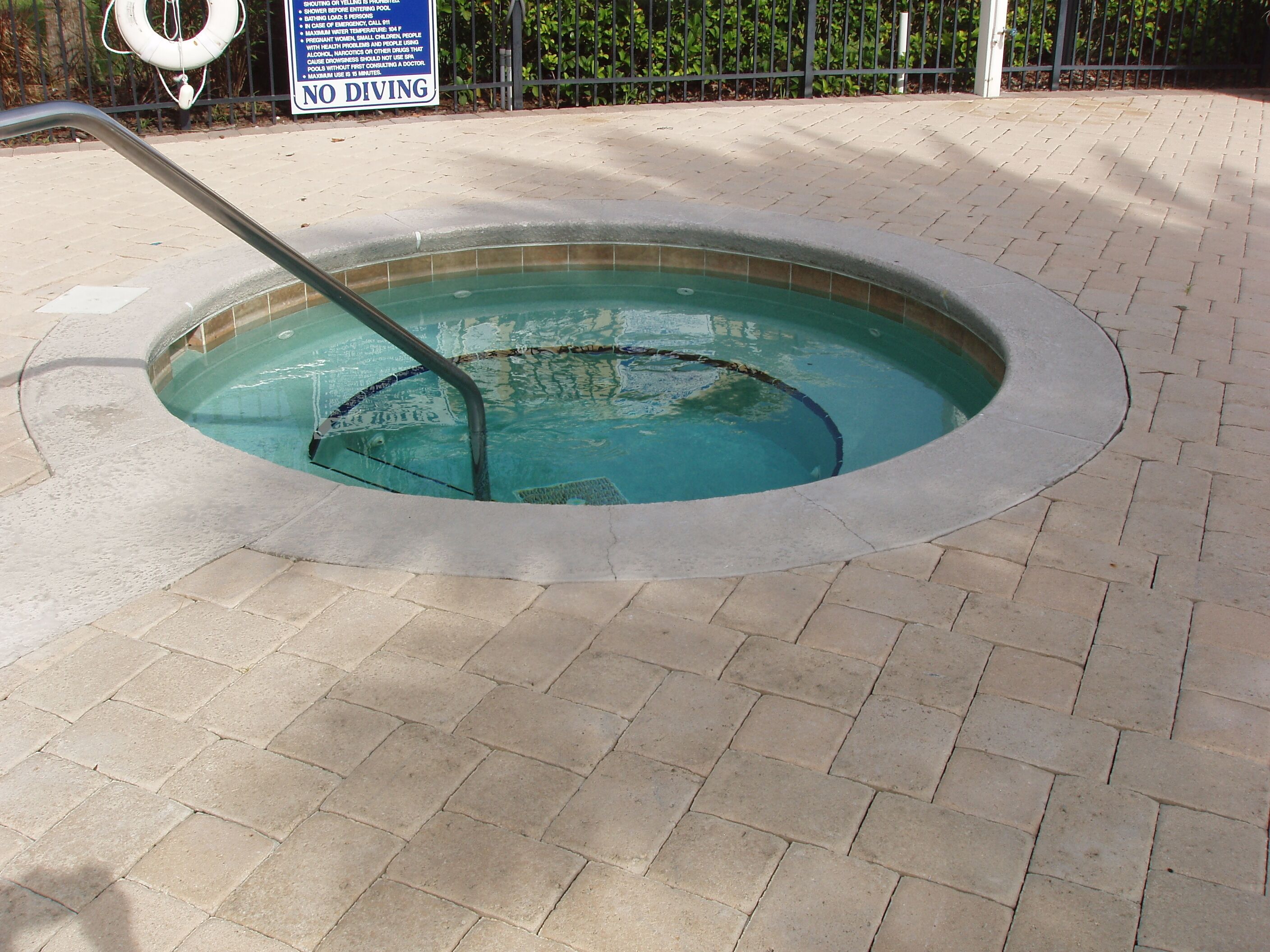 A circular pool with a metal ladder, surrounded by a brick walkway.