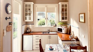 Una cucina con mobili bianchi, un forno a microonde e un lavandino. Si vede una finestra con vista su piante.