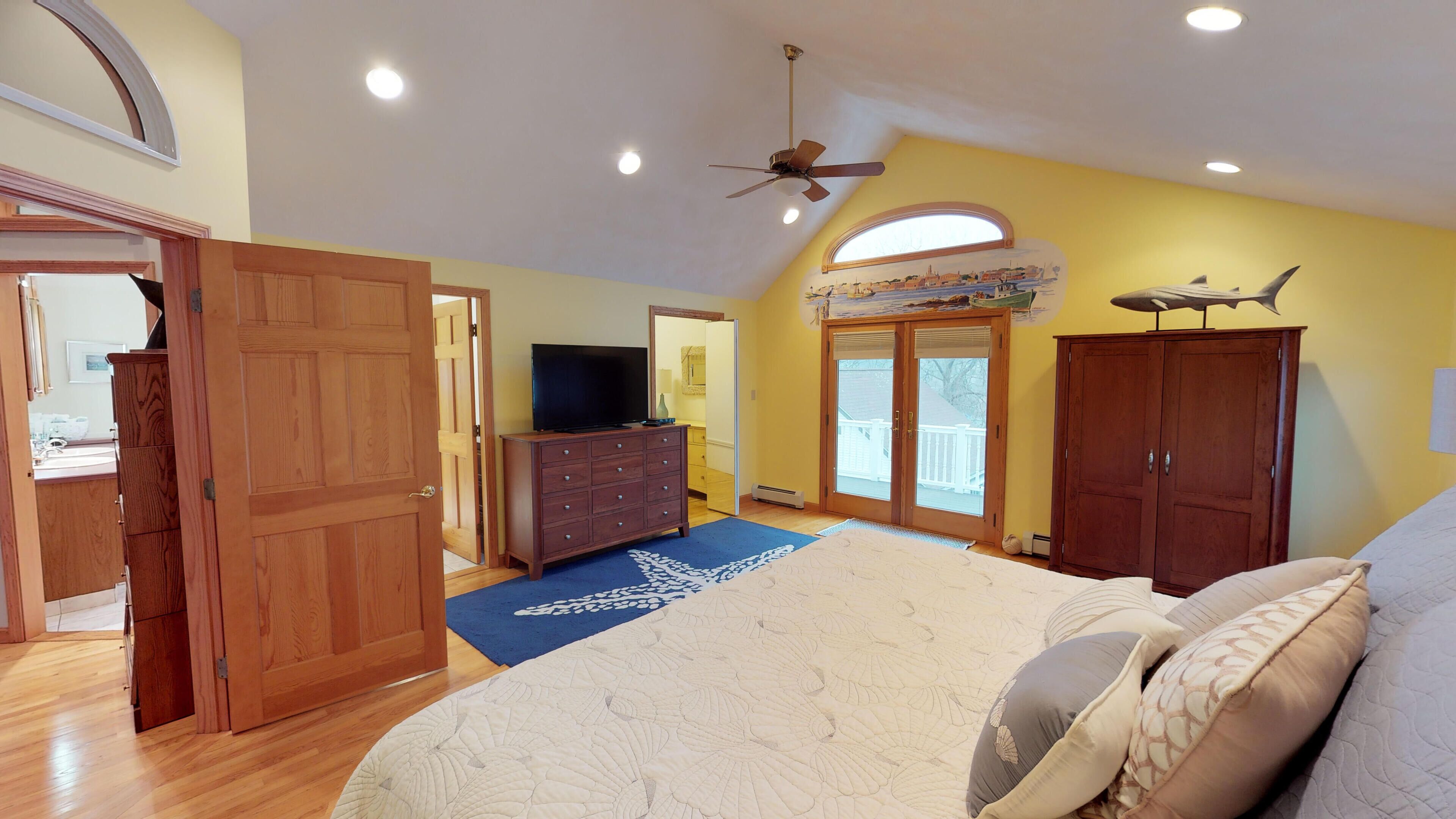 A bedroom with a large bed, wooden wardrobe, a television on a dresser, and a ceiling fan.