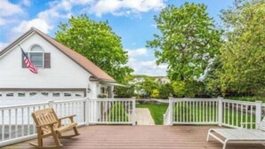 A house with a white exterior, a porch with a wooden deck, and a flag.