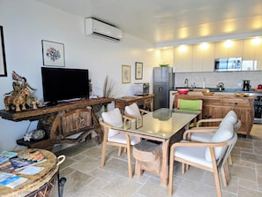 Eine moderne Küche mit Flachbildfernseher, Kühlschrank und Mikrowelle. Ein Essbereich mit Glastisch und Holzstühlen ist ebenfalls vorhanden.