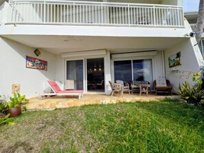 Un edificio residencial con balcón, puerta corredera de vidrio que da a un área de comedor al aire libre y un pequeño jardín.